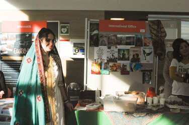 A young woman stands smiling in traditional dress in front of the Iranian country stand at the international "Marketplace of Opportunities"__A young woman stands smiling in traditional dress in front of the Iranian country stand at the international "Marketplace of Opportunities"