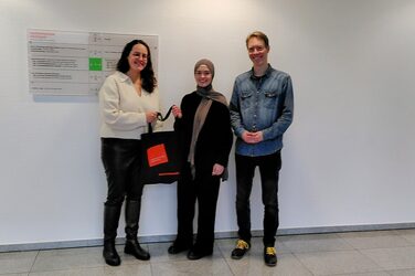Preisübergabe an eine Teilnehmerin des Gewinnspiels: Ein Mitarbeiter des International Office und eine Mitarbeiterin der Auslandsgesellschaft überreichen der Gewinnerin eine gefüllte Stofftasche
The winner of the stamp rallye receives her prize: Employees of the International Office and Auslandsgesellschaft hand out a filled tote bag to a young female student