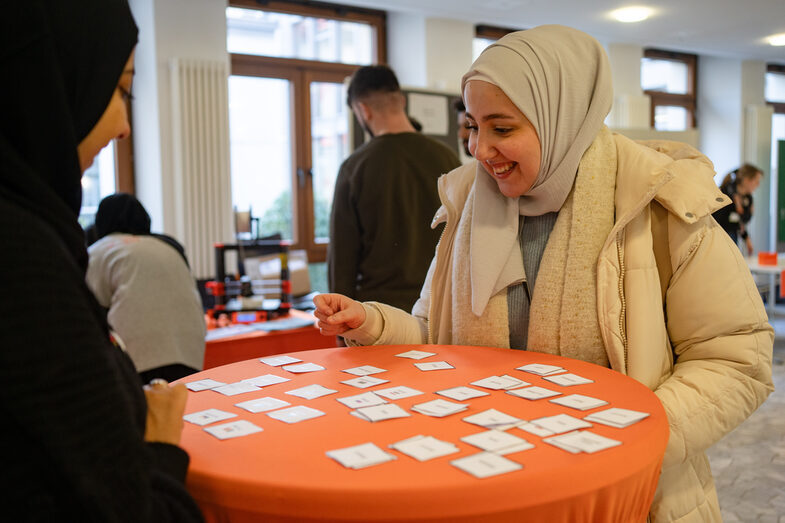 Zwei junge muslimische Frauen spieeln an einem Stehtisch, beim Welcome Event der Internationalen Woche ein Spiel und haben Freude daran.__Two young Muslim women play a game at a bar table at the Welcome Event of the International Week and enjoy it.