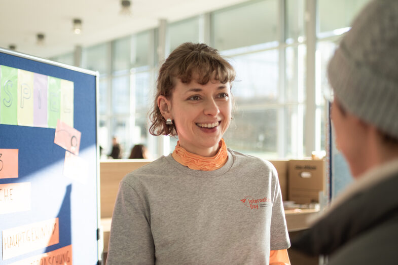 A young woman hands a person a prize from a competition and the sun shines into the room.