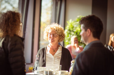 Three people are talking at a bar table in the sunshine, at the welcome event of the international week.In the background are windows__Three people are talking at a table in the sunshine, at the welcome event of the international week.In the background are windows