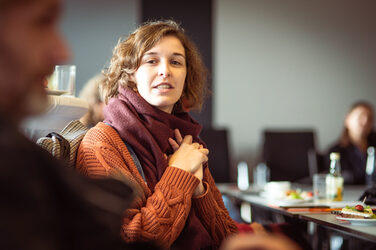 Woman with scarf and orange knitted sweater talking with man in blur on left__Woman with scarf and orange knitted sweater talking with man in blur on left