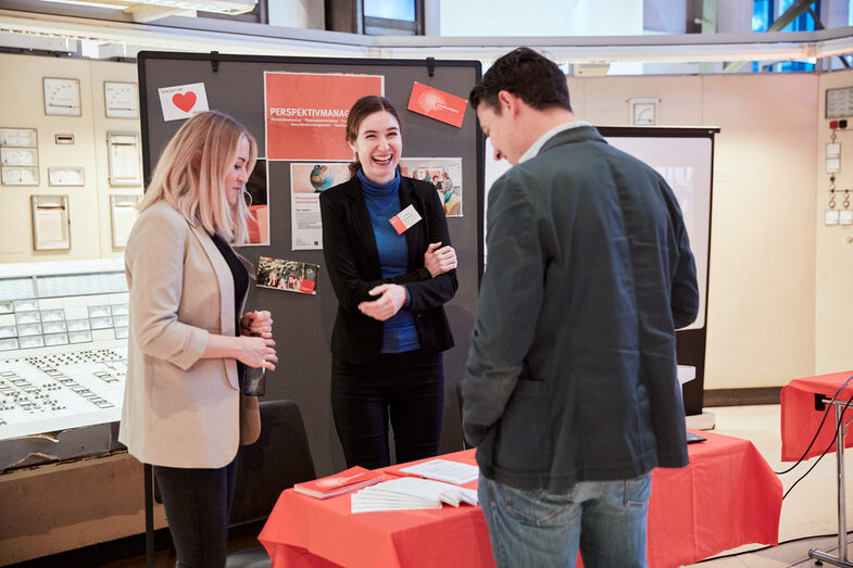 Two female university employees in conversation with a visitor at an info table at the event venue DASA.