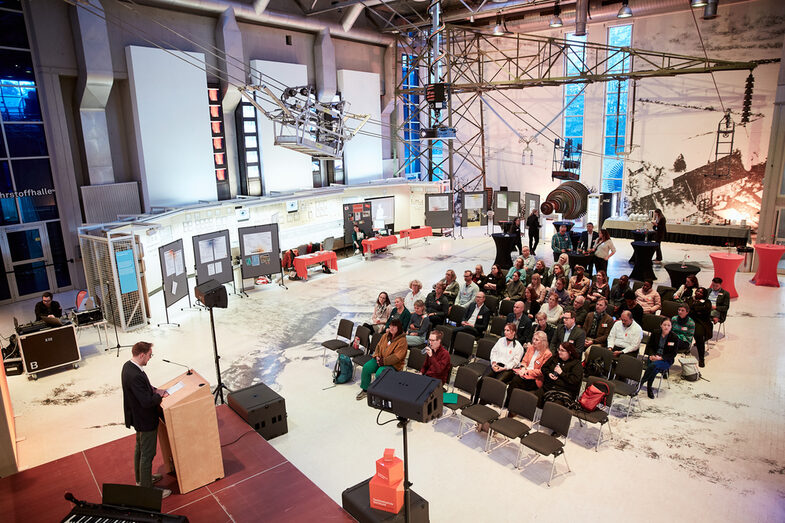 Ein Panoramablick von oben auf den gesamten Veranstaltungsraum in der DASA, mit Bühne, Posterausstellung, Bestuhlung und Dekoration__A panorama view of the whole venue from above, with stage, poster exhibition, seating and decoration