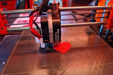 In einem 3D-Drucker entsteht ein orangefarbenes Plättchen in Herzform