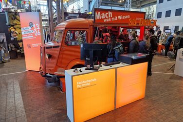 Vor dem HY-Oldtimer der FH steht unter anderem eine orange beleuchtete Theke mit einem Computer..