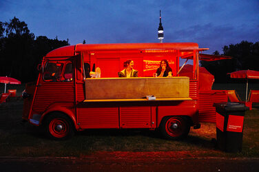 Der Citroën HY beim PSD-Bank-Kino 2019. Das Bild zeigt eine Abendstimmung. Der HY ist erleuchtet, die Seitenwand hochgekappt. Zwei Studierende stehen im inneren und schauen hinaus.