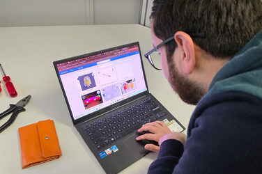 A person is operating a laptop; several images from an image database can be seen on the screen. Tools lie next to it.