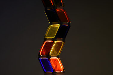 Night shot of a colorfully illuminated, sculptural lamp on a wooden base