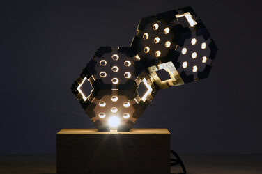 Nachtaufnahme einer erleuchtenden, skulpturalen Hexagon Leuchte auf einem Holzsockel mit generativ gefertigten Elementen