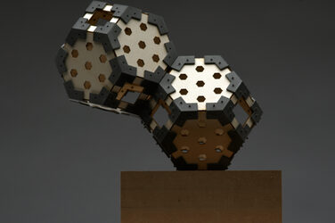Modell einer skulpturalen Hexagon Leuchte auf einem Holzsockel mit generativ gefertigten Elementen vor grauem Hintergrund