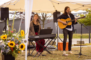 Zwei Personen mit Keyboard und Gitarre machen Musik unter einem Sonnenschirm.