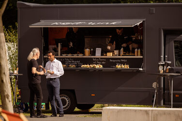 Zwei Personen stehen mit Essen in der Hand vor einem Foodtruck.