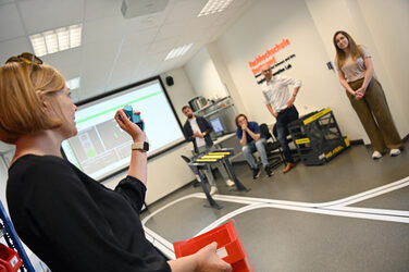 Eine Person seht in einem Labor und hält Items in der Hand. Sie erklärt etwas. Andere Personen hören ihr zu.