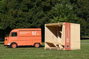 The Fachhochschule Dortmund's wooden seating cube is located in a green area near the Westfalenhallen subway station.