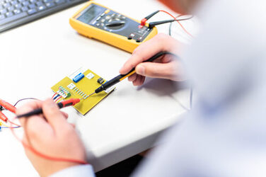 Photo of a voltage measurement across a resistor on a circuit board being carried out by an employee.