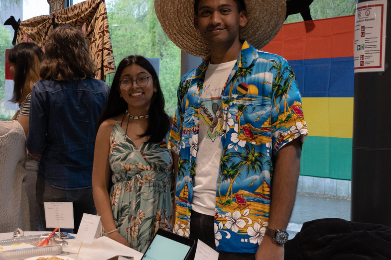A cultural stand from Mauritius. On the table is a rich buffet with various typical dishes and postcards. Behind the table are two students looking after the stand.