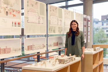 Graduate Silvia Wolf in front of the plans of her Bachelor's thesis on the galleries of the faculty.