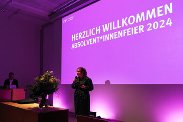Chancellor Svenja Stepper during her speech in front of the colorful illuminated screen in the lecture hall.