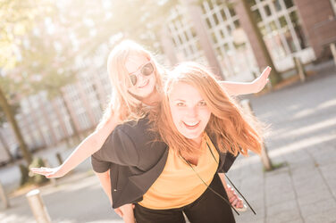 Photo of a woman with a little girl whom she is carrying piggyback. The girl is wearing orange sunglasses. __ A woman piggybacks a little girl. The girl is wearing orange sunglasses.