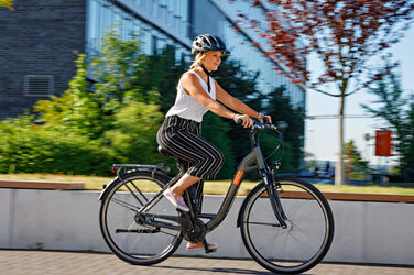 Foto einer jungen Frau, die mit dem Fahrrad über den Campus fährt. Sie trägt einen Helm.__ Young woman rides a bike across campus.