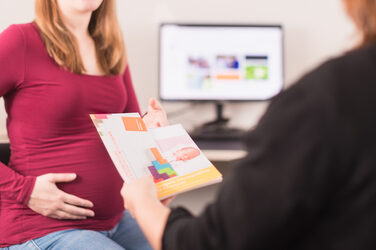Foto einer schwangeren Frau, die einer Mitarbeiterin aus dem Familienservice gegenüber sitzt und einige Flyer zum Thema „Vereinbarkeit von Familie und Studium“ entgegen nimmt.