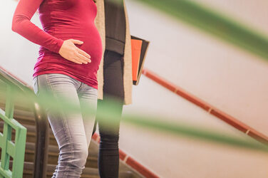 Photo of a student with a baby bump. She is walking next to a fellow student in the building and clutching her stomach. The heads of the people are not in the photo __Photo of a female student with baby bump. She walks next to a fellow student in the building and grabs her belly. Heads of the people are not included in the photo.