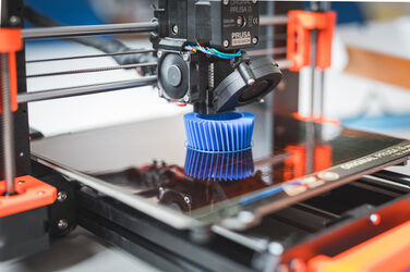 Nahaufnahme eines 3D-Druckers, der ein blaues Objekt druckt.