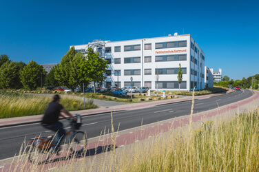 Building photo with "Fachhochschule Dortmund" logo on building 38b - from a distance. Cyclist enters the picture on the left.