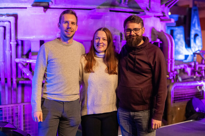 Photo of a female and two male persons smiling standing into the camera.