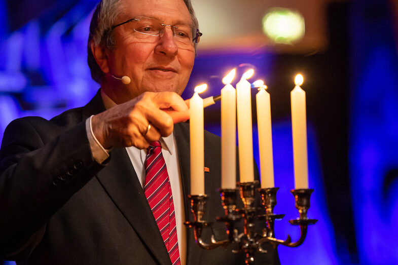 Photo of a male person. This person is lighting five candles in a candlestick.