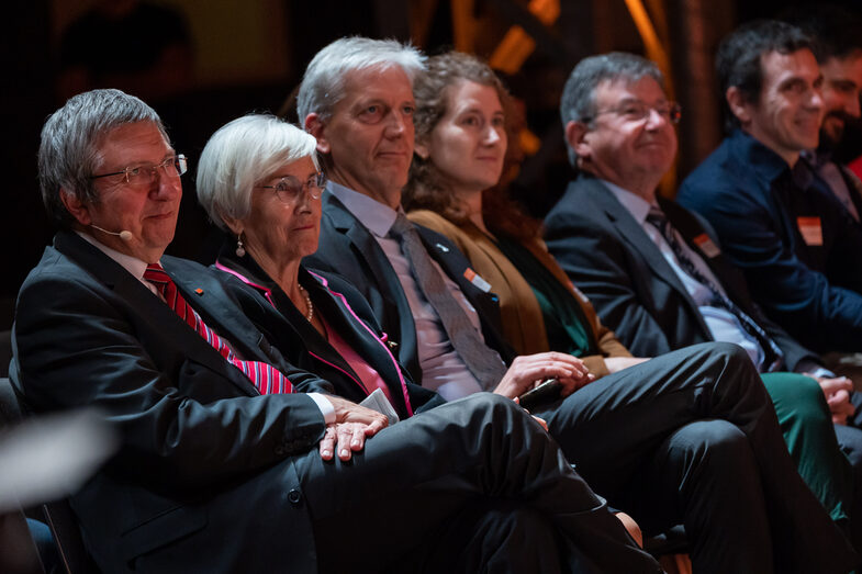 Photo of five male and two female persons sitting and looking in one direction.