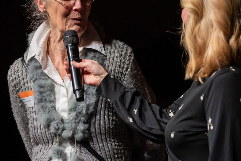 Photo of two female persons. One person is speaking into a microphone.