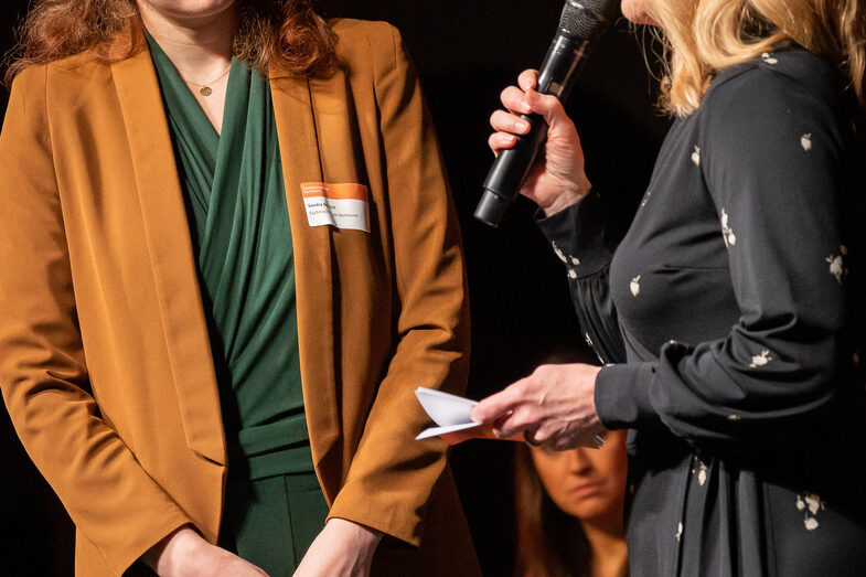 Foto von zwei weiblichen Personen. Eine Person spricht in ein Mikrofon.