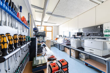 Raumaufnahme der Hardeware-Werkstatt. zu sehen sind verschiedene Werkzeuge auf der Werkbank links und rechts verschiedene Drucker.