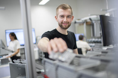 Foto von einem Student, der nach einem Einzelteil aus einem Behälter greift, am Arbeitsplatz im Lean Labor.