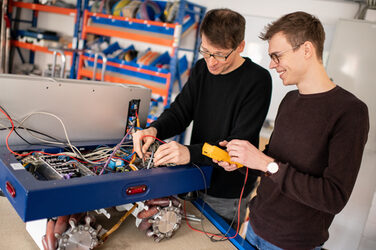 Photo of 2 people in a workshop working at a workbench.