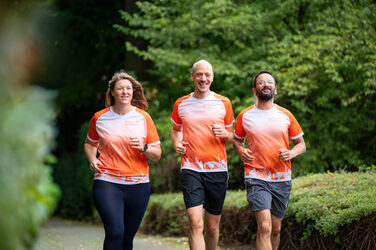 Drei joggende Personen draußen im Grünen, die ein FH-Dortmund-Laufshirt tragen