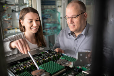 Photo of a trainee with her practice supervisor. They are looking at a server together. The trainee explains her approach to her task with a pen.