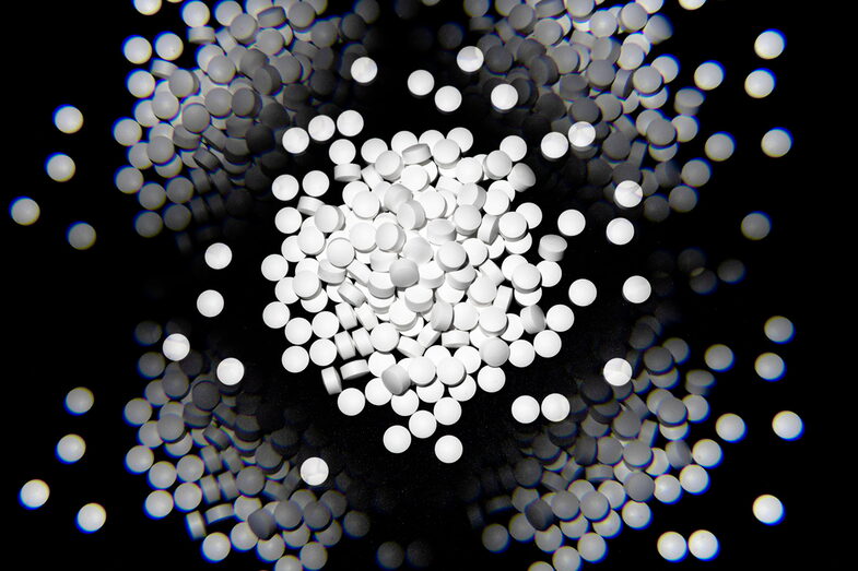 Das Schwarz-Weiß-Foto zeigt ein Häufchen weißer Pillen auf schwarzem Grund. Am Rand sind mehrere Spiegelungen des Häufchens zu sehen.