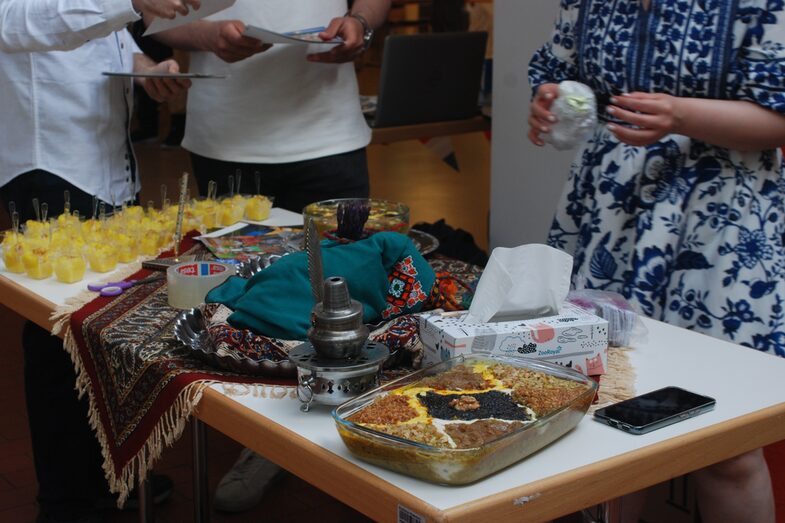 stand at a cultural fair "Iran": People stand around a table on which is food.