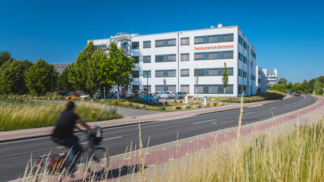 Gebäudeaufnahme mit Logoanbringung "Fachhochschule Dortmund" am Gebäude 38b - aus der Ferne. Fahrradfahrer fährt links ins Bild.