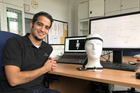 The doctoral student Puian Tadayon sits at a with a wired model of a head and a computer on it.