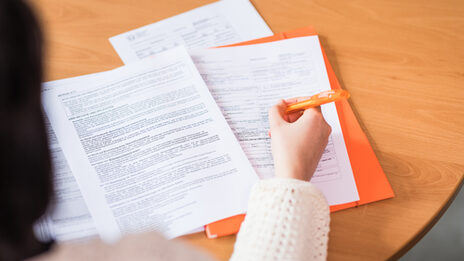 A cropped photo of a person filling out a stack of documents.