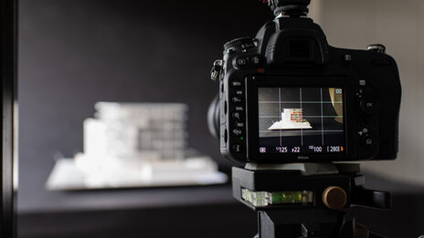 Foto von enem Bildschirm einer Kamera, die auf ein Modell eines Gebäudes vor einem schwarzen Hintergrund gerichtet ist.