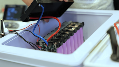 View of a battery storage system with several cells plus electronics in a safety box with an open lid.