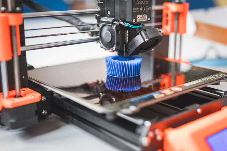 Photo of a 3D printer printing a blue object. __ <br>3D printer prints blue object.