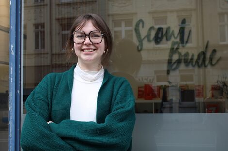 Portrait photo of Hannah Sikau standing outside the window of the Hochschule vor Ort