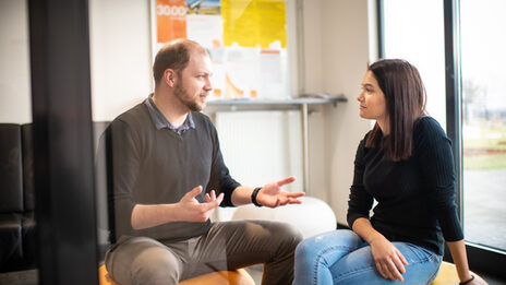 Ein TalentScout und eine Schülerin, die auf Sitzsäcken sitzen und sich unterhalten. Vor ihnen liegen auf einem Beistelltisch einige orangefarbene Mappen.