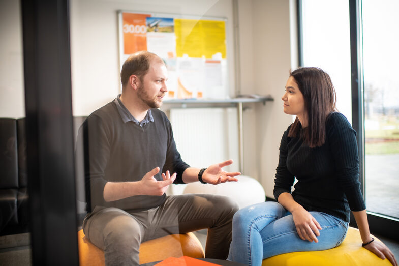 A TalentScout and a student sitting on beanbags and chatting. In front of them on a side table are some orange folders.